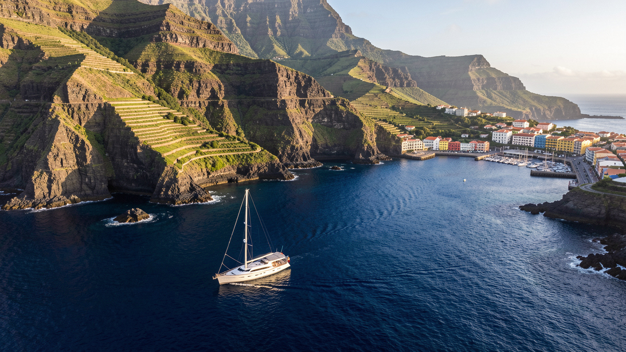 Voilier naviguant le long de la côte volcanique de Madère, entre falaises verdoyantes, criques et port pittoresque.